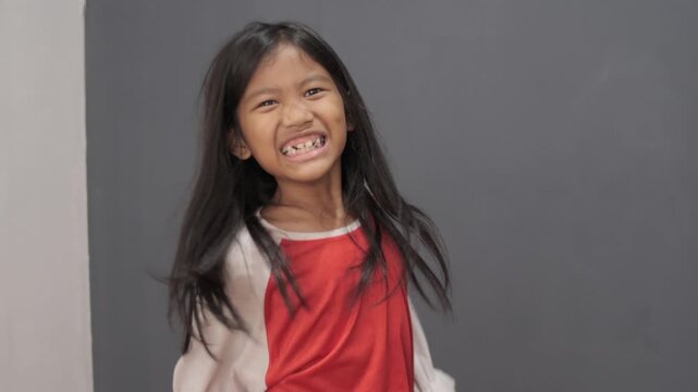 Frustrated Asian little girl holding her head with stressed expression. Portrait of stressed elementary student feeling overwhelmed and tired. Childhood mental health, headache, and academic burnout