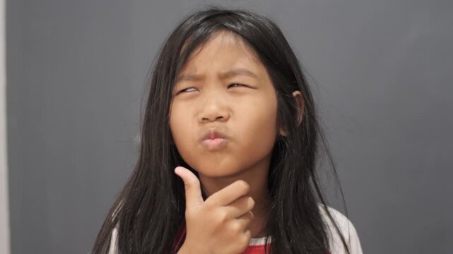 Thoughtful little Asian girl thinking with hand on chin, pensive child looking up having a doubt or making a decision, imagination, problem solving and education