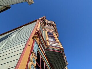 Upward view of ornate Victorian building with colorful detailed facade against blue sky,...