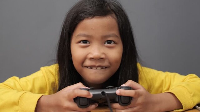 Excited little Asian girl playing video games with controller, happy child smiling and cheering while gaming, kids technology and home entertainment