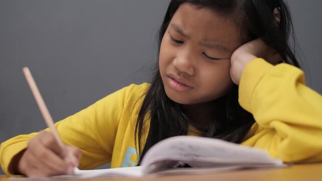 Stressed little Asian girl with glasses crying while studying, unhappy child having headache or difficulty with homework, academic pressure and learning disability