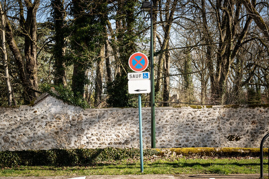French roadside sign showing stopping and parking prohibited, with a supplementary sauf (meaning except in french) plate exempting vehicles used by disabled persons, a symbol of handicap parking spot.