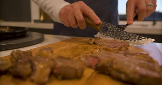 Low, closeup shot of cook quickly cutting up steaming steak on wood board