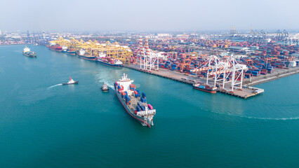 Massive container ship navigating near a busy commercial port terminal loaded with colorful...