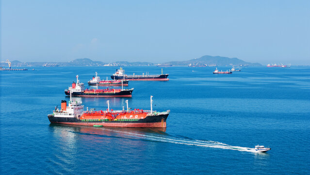LPG gas and oil tanker ships anchored in the ocean, with a fast patrol boat in the foreground. Global energy transport, war energy crisis, and Strait of Hormuz blockade concept.