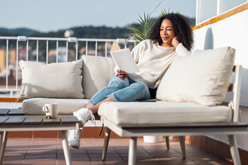 Fototapeta premium Relaxing woman reading a book while resting on the couch on her balcony at home