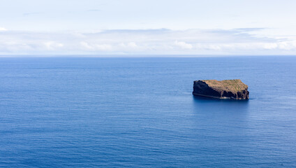 Naklejka premium Small rocky islet in the Atlantic Ocean. San Miguel Island, Azores, Portugal. Volcanic landscape surrounded by blue sea.