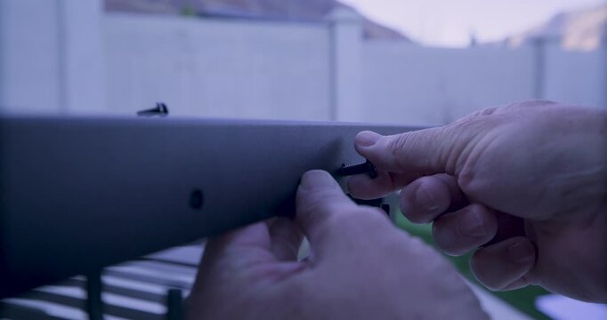 Man's hands attaching hooks to metal structure and putting screw in hole by hand - closeup