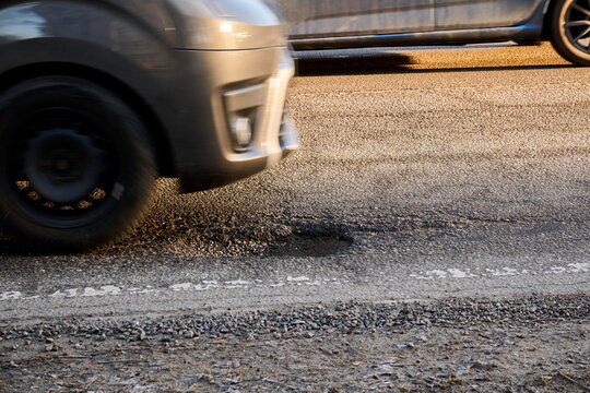 Car Driving Past a Dangerous Pothole on a Damaged Asphalt Road