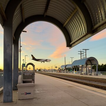 LOS ANGELES, CA, DEC 17, 2025: empty Metrolink and Amtrak platform at golden-hour sunset with a UPS cargo plane flying low overhead beneath an arched station canopy at Burbank Airport
