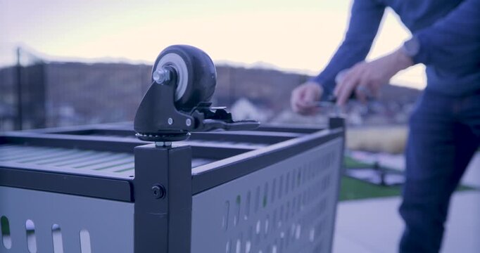 Handheld, rack focus shot on wheels of upside down grill as man screws one on