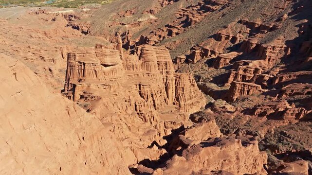 Vast desert canyon in Kyrgyzstan showcases dramatic rock formations shaped by erosion. Crane down tilt up aerial camera movement.