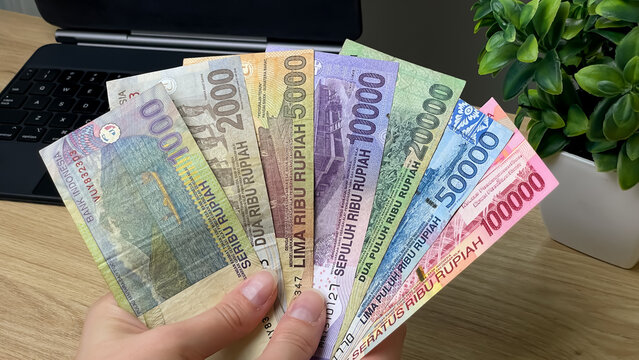 A man holds Indonesian rupiah banknotes of various denominations on his desk. Conceptual concepts of spending, budgeting, travel, and financial control.