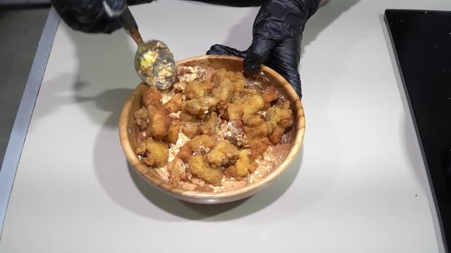 Gloved Chef Hands Mixing Crispy Fried Chicken in Wooden Bowl