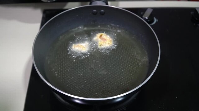 Gloved Hand Deep Frying Pieces of Chicken in Hot Sizzling Oil