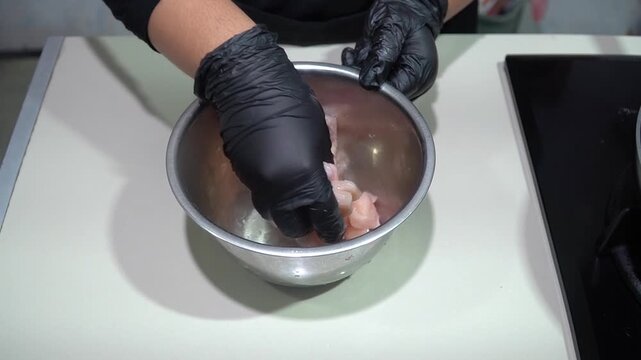Gloved Chef Marinating Raw Chicken Pieces in Stainless Steel Bowl