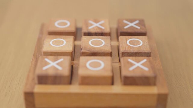 Hand holding and playing wooden block of tic tac toe game. A completed game of noughts and crosses or Xs and Os game. Challenge, Competition, winning, tactic, strategy and recreation concepts
