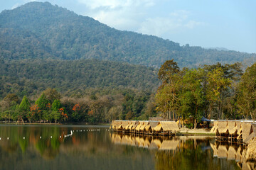 Fototapeta premium Floating thatched huts along the lake with mountain forest and clear reflections