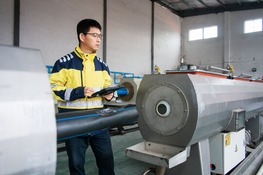 Worker operating pipe extrusion machine during industrial production in factory workshop