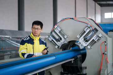 Worker operating pipe processing equipment while conducting inspection in factory