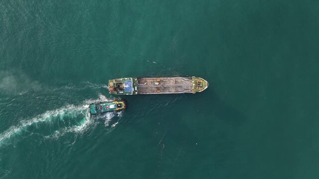 Aerial top view of a tugboat assisting a barge at sea