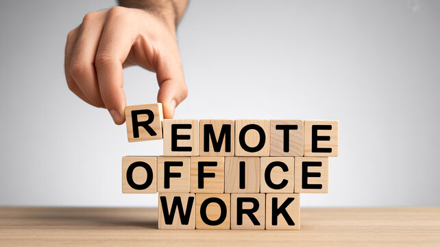 A hand places the letter R wooden block completing REMOTE OFFICE WORK on a table under bright light conceptualizing flexible employment for modern bus