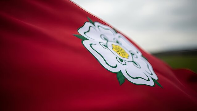Yorkshire Rose flag rippling in the wind against a cloudy sky, outdoors.