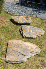 Fototapeta premium Natural greywacke stone slabs used as stepping stones on grass in garden landscape design. Rustic outdoor path stones for backyard walkway.
