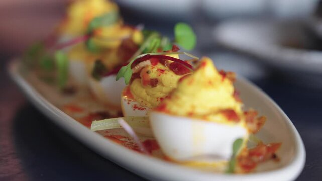 4K slow motion footage of delicate deviled eggs topped with microgreens served on an oval white plate at an elegant brunch restaurant, highlighting gourmet presentation.