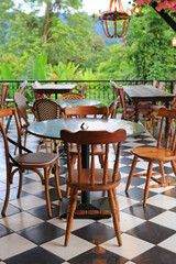 Fototapeta premium Empty bistro tables and woven chairs sit quietly on a balcony, waiting for guests to enjoy a meal overlooking the lush tropical forest and distant mountains.