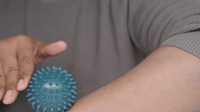 A person uses a green spiked massage ball to relieve tension and stimulate blood flow in their forearm with repetitive rolling motion