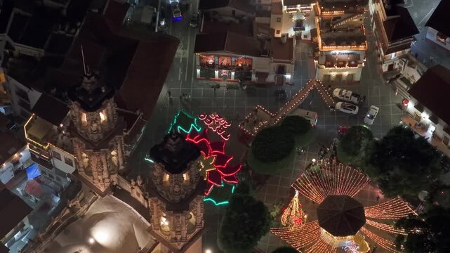 Aerial view of the giant poinsettia in front of the illuminated Santa Prisca temple at night in Taxco with cobblestone streets in Guerrero, Mexico