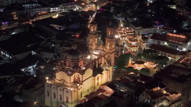 Aerial telephoto tilt-down view of the Santa Prisca temple at night with illuminated streets in Taxco, Guerrero, Mexico