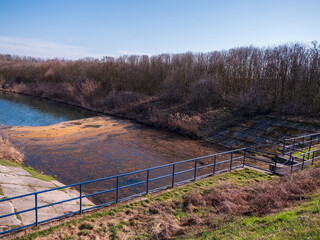 Fototapeta premium Danube canal near Čilistov and Samorin, Slovakia, polluted water surface with algae, riverbank with railing and trees, environmental problem in natural landscape.