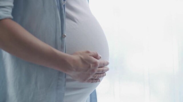 Stunning shot of pregnant woman gently holding her belly in bright room.  Happiest moment for a couple expecting baby in their life. 