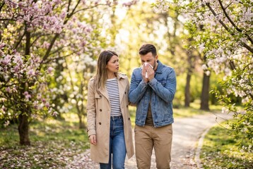 Fototapeta premium young man and woman blooming garden, man sneeze from seasonal allergy