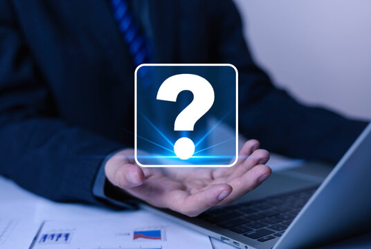 Businessman holding glowing question mark icon over laptop, symbolizing problem solving, support, FAQ, customer service, uncertainty, decision making and digital technology concept in modern office.