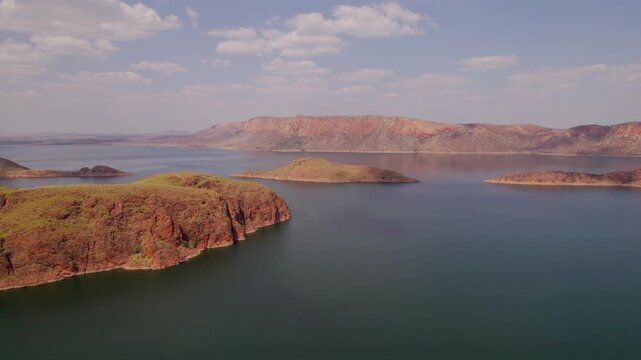 Drone flying forward and descending over the turquoise waters of Lake Argyle in Western Australia, revealing rugged islands and vast remote Kimberley landscape under soft daylight.