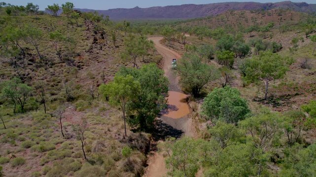 Drone view of a 4x4 van crossing a shallow creek on the remote track toward Purnululu National Park (Bungle Bungles) in the Kimberley region of Western Australia.