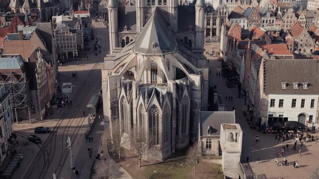 A dramatic top-down aerial view from the Ghent Belfort reveals the intricate Gothic architecture of Sint-Niklaaskerk below, with flying buttresses and pointed spires surrounded by the historic city ce