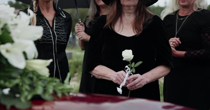 Sad, casket and people at graveyard for funeral, goodbye and mourning for loss, roses and depression. Cemetery, family and burial for death, flower bouquet and memorial service with grief or greeting