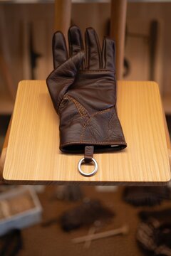 Single brown leather falconry glove with metal jess ring on wooden display