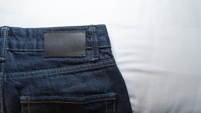 Close-up of back waist with blank black leather label on dark blue denim jeans. Isolated on white fabric background.