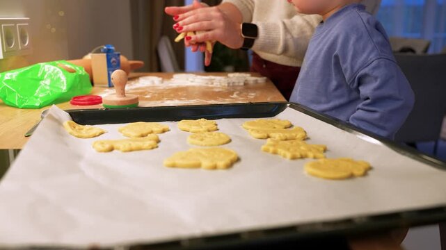 Warm, intimate scene of cookie baking at home. Focus on hands crafting dough shapes while child eagerly watches, all set in cozy kitchen atmosphere. Soft lighting highlights textures.