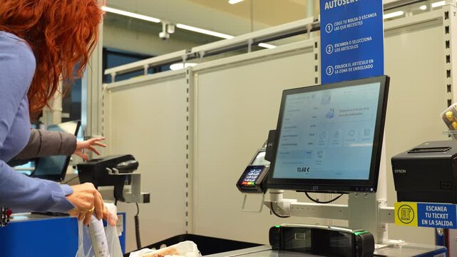 Woman scans final product at a supermarket self-checkout machine and bags her groceries