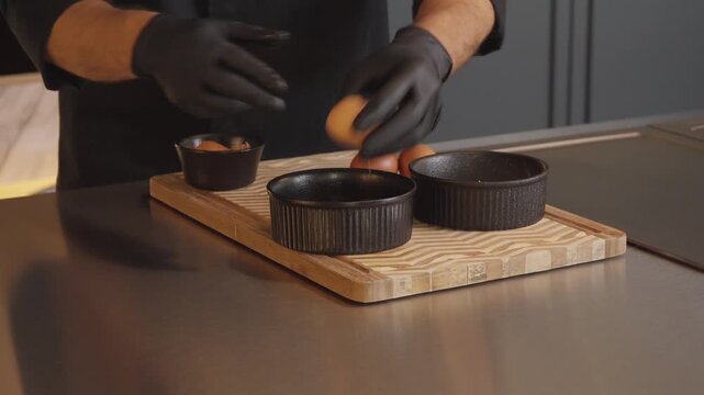 Gloved chef cracking eggs into baking ramekins on kitchen counter