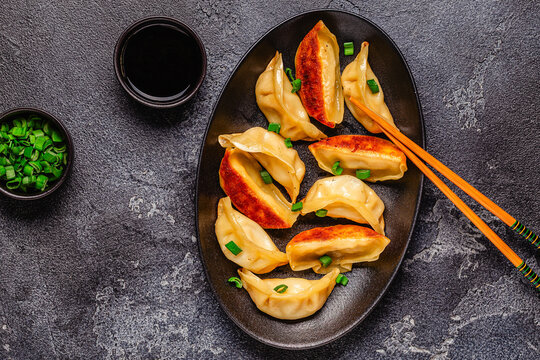 Dumplings are served on a black plate with green onion