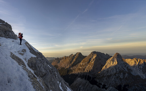 Hiker walking along a snow-covered mountain ridge at dawn