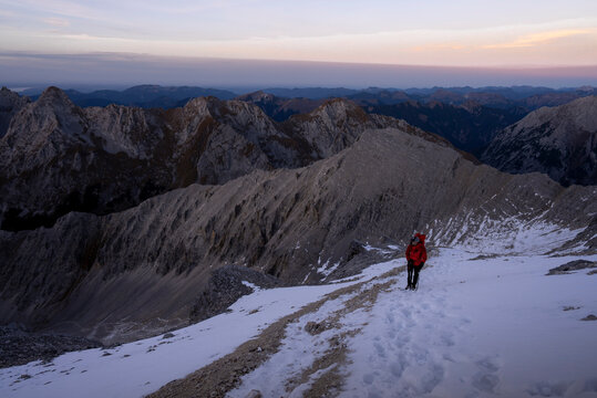 Hiker walking along a snow-covered mountain ridge at dawn