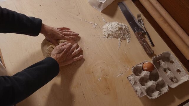 Top-down view of a Romagna cook kneading fresh cappelletti dough by hand on a wooden table. Traditional Italian pasta-making with flour, eggs, and simple kitchen tools.